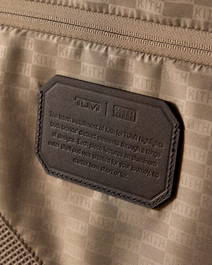 Close-up of a tan fabric with a leather patch showing the collaboration logo "TUMI KITH" and text about their design partnership