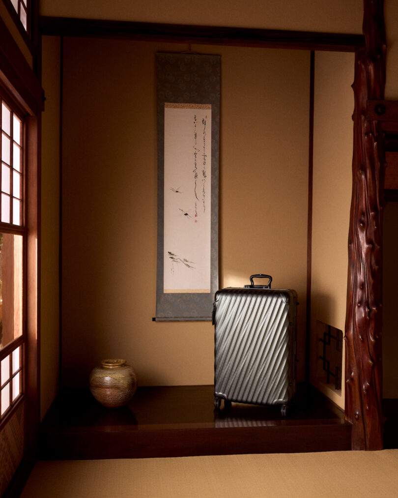 A suitcase is placed in a traditional Japanese room with a scroll hanging on the wall and a decorative pot nearby