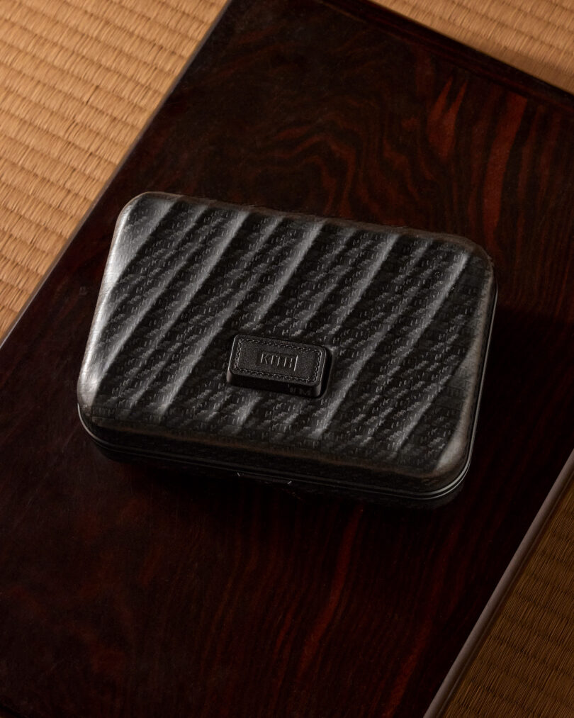 A black textured rectangular case sits on a dark wooden surface