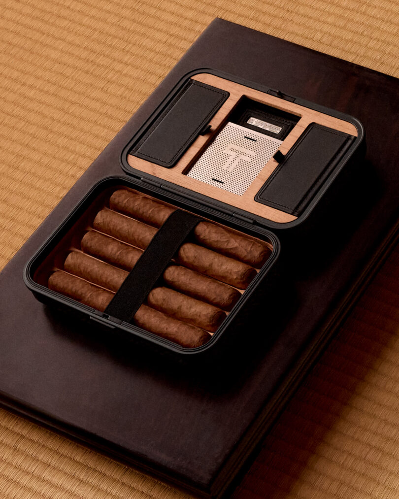 A cigar case holding six cigars and a metal accessory, placed on a textured mat