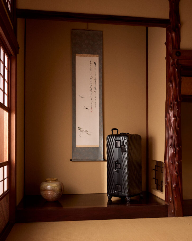 A black suitcase stands in a traditional Japanese room with a hanging scroll and vase