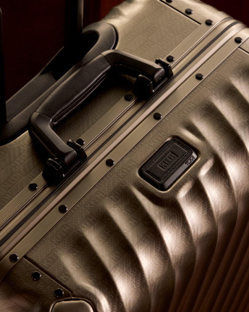 Close-up of a textured, hard-shell suitcase with a black handle, metallic accents, and a visible brand logo