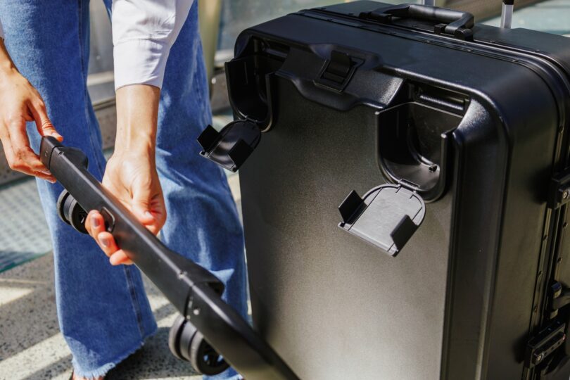 Person assembling the handle of a large black suitcase on a sunny day