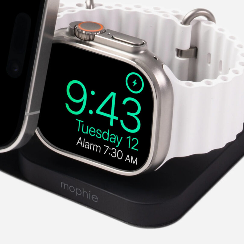 Smartwatch with a white band on a charging dock displays time as 9:43 and alarm set for 7:30 AM.