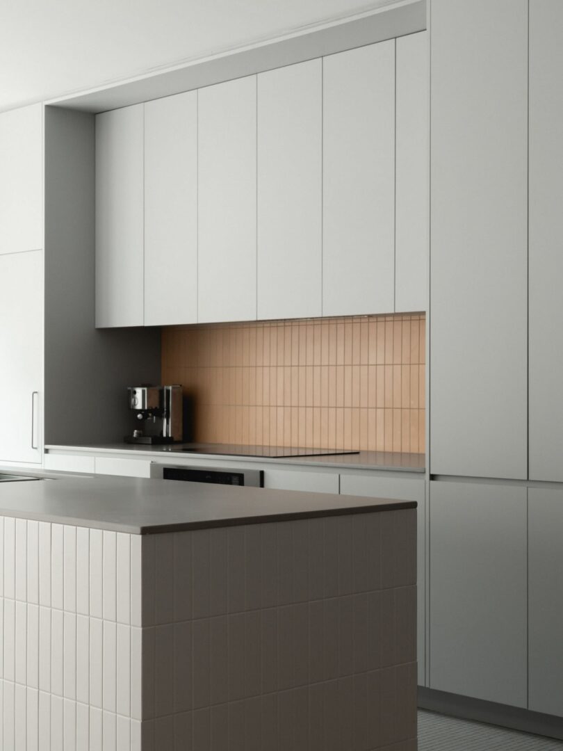 Modern kitchen with white cabinets, a beige tiled backsplash, and a gray island countertop. A coffee machine is on the counter.