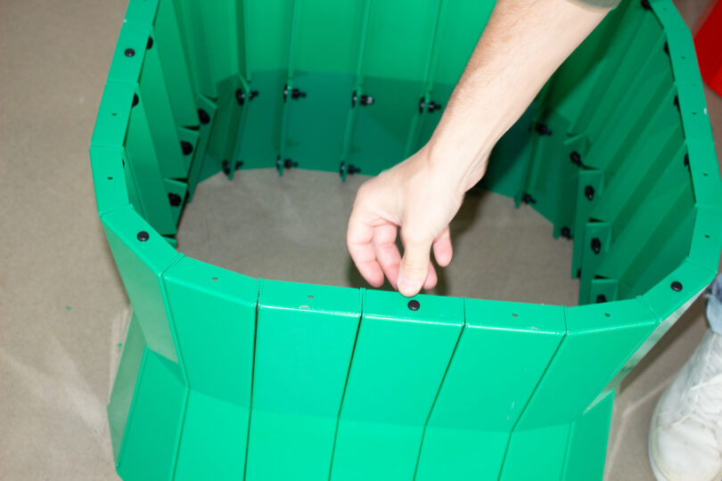 A person assembles green plastic panels, fastening them together with black connectors on a flat surface