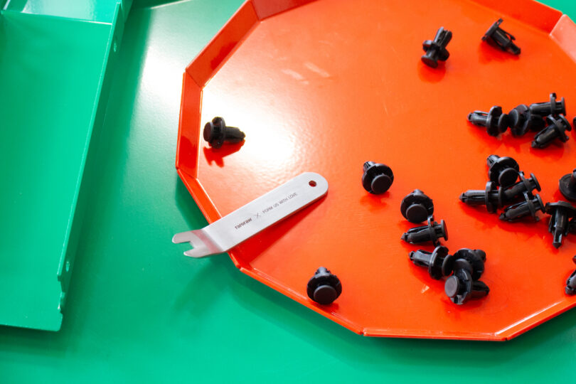 Orange tray with black plastic fasteners and a metal tool on a green table