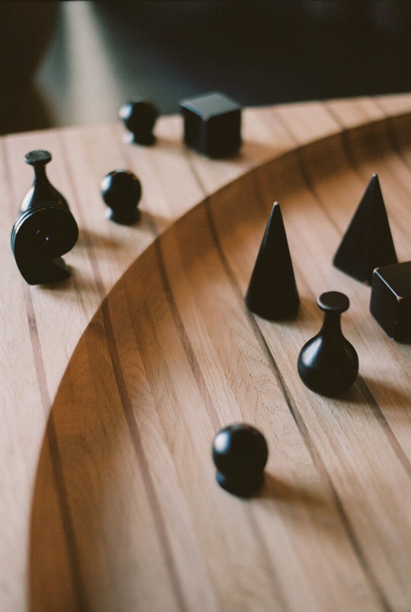 A curved wooden table with various black three-dimensional shapes, including cones, spheres, and cubes, scattered across its surface