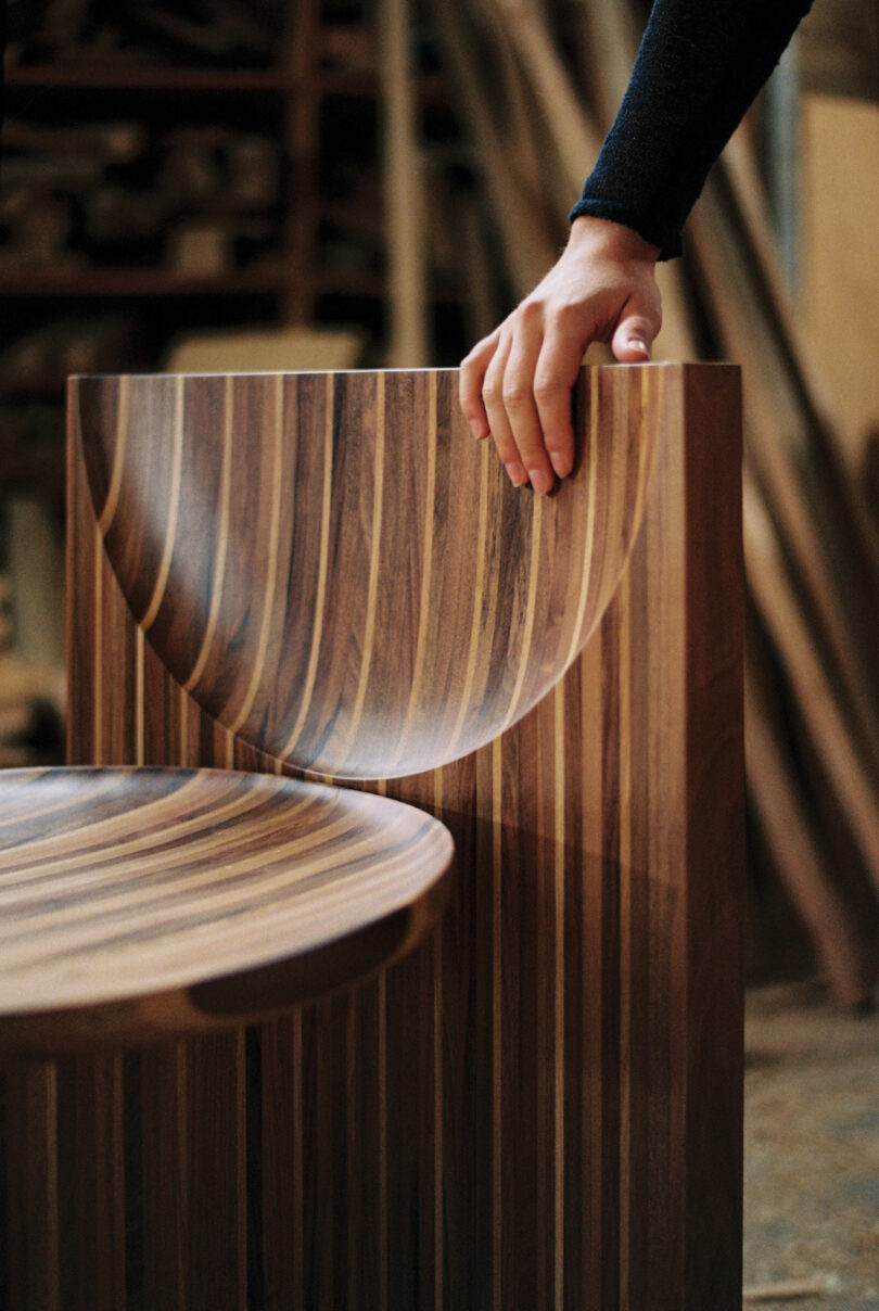 A hand rests on a striped wood chair with a curved back in a workshop setting