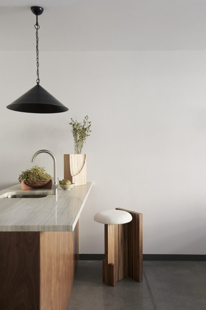 Minimalist kitchen with a marble countertop, wooden stool, pendant lamp, and decorative plants on the counter