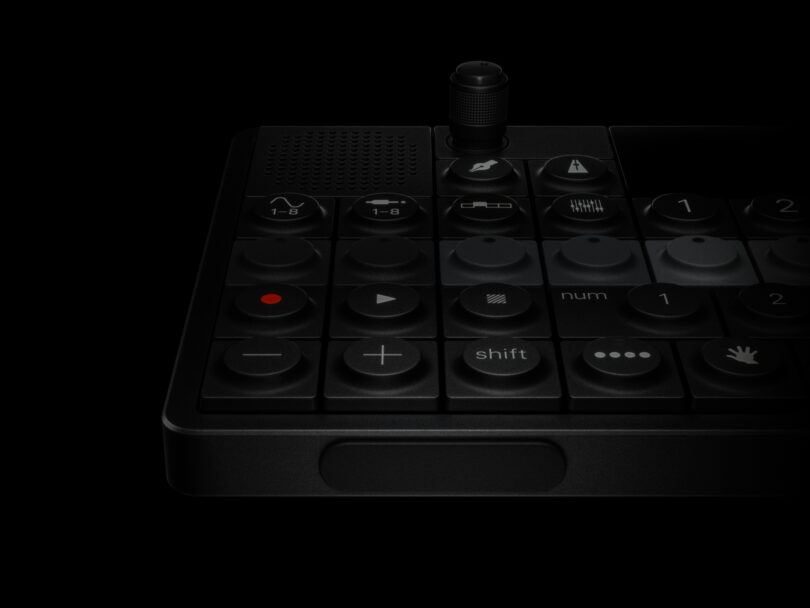 Close-up of a black electronic device with various buttons, including play, pause, and shift functions, against a black background.