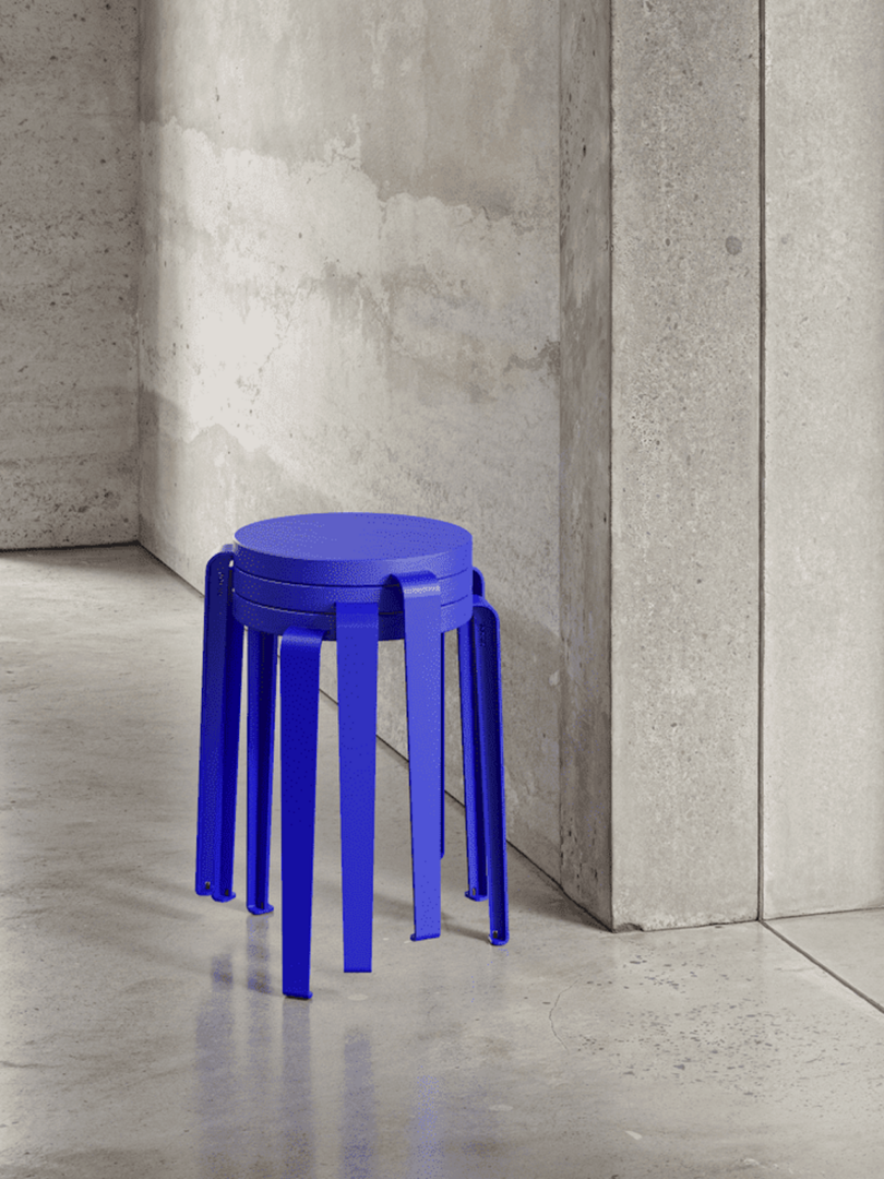 A modern, blue stool with multiple legs placed against a concrete wall in a minimalist setting