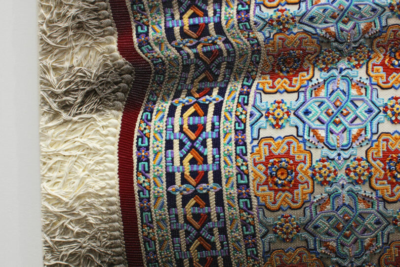 Intricately woven textile featuring bold geometric and floral patterns in vibrant colors, with a textured border on the left side.