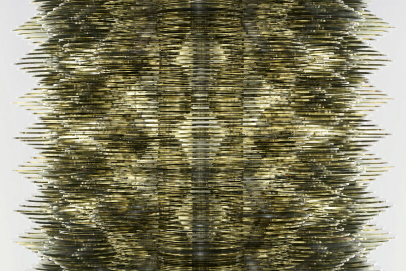 Close-up of a metallic, symmetrical, layered structure with a reflective surface, resembling a complex vertical wave pattern.