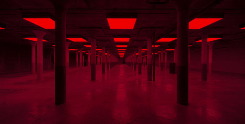 A dimly lit room with red fluorescent ceiling lights and multiple columns arranged in rows.