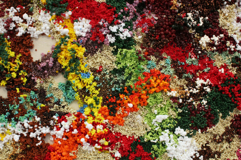 A colorful assortment of small, scattered beads in various colors, including red, green, yellow, and white, on a flat surface.