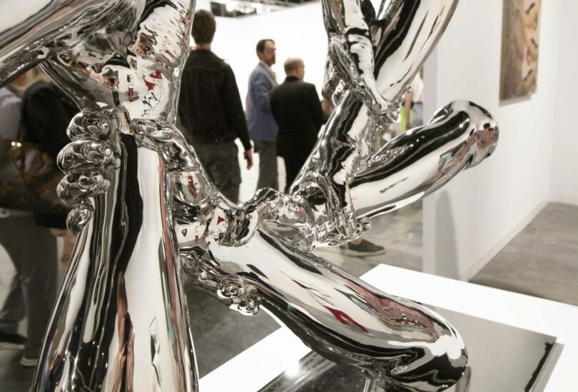 Visitors walk close to reflective sculpture of hands.