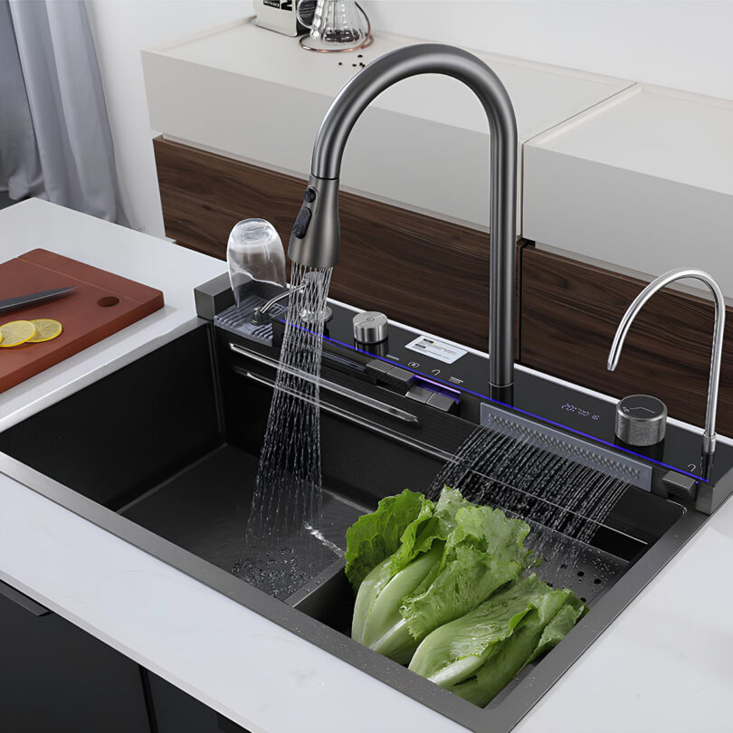 Modern kitchen sink with a high-arc faucet spraying water over lettuce. Cutting board with sliced lemons and a small faucet for filtered water are visible.