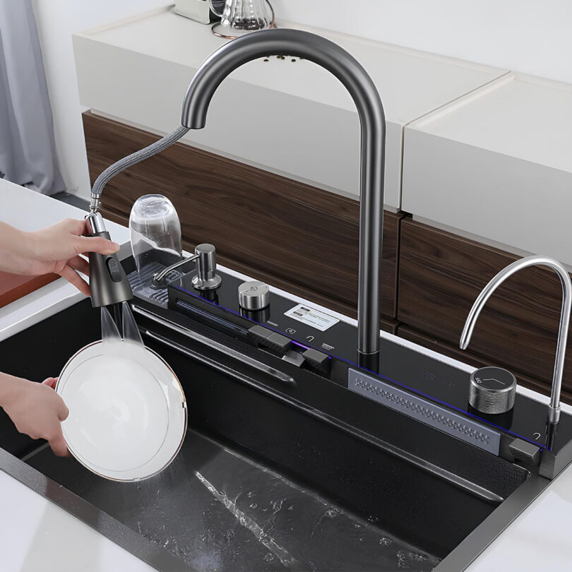 Person rinsing a white plate under a detachable kitchen faucet in a modern sink setup.