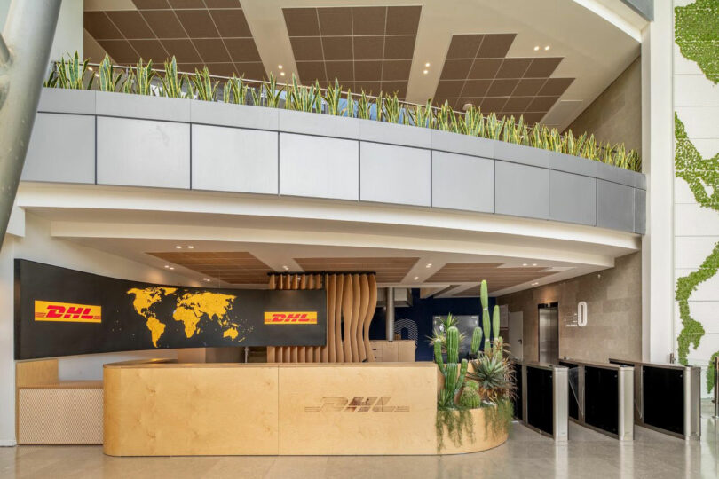 Hall du bureau DHL avec un comptoir de réception en bois, une carte du monde au mur, des plantes en pot et une décoration moderne.