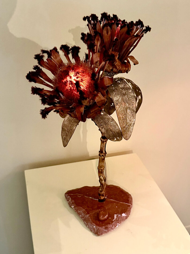 A decorative lamp shaped like a flower with metal petals and a rocky base, illuminated from within, displayed on a white surface.