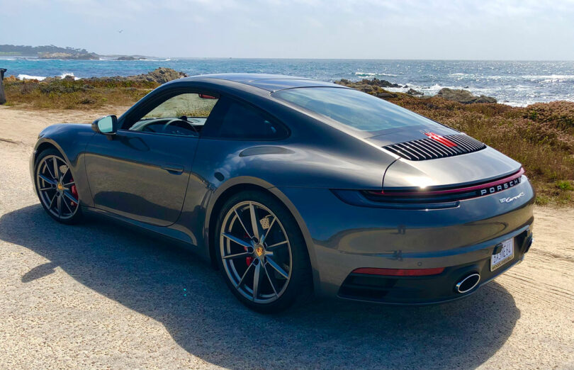 Une élégante voiture de sport grise, rappelant les designs innovants de Dan Harden, se trouve élégamment près d'une côte rocheuse avec le vaste océan qui s'étend au loin.