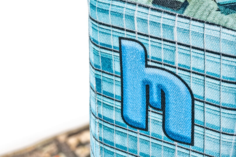 Close-up of a patterned fabric with a blue lowercase "h" design against a background of blue and green checkered squares.