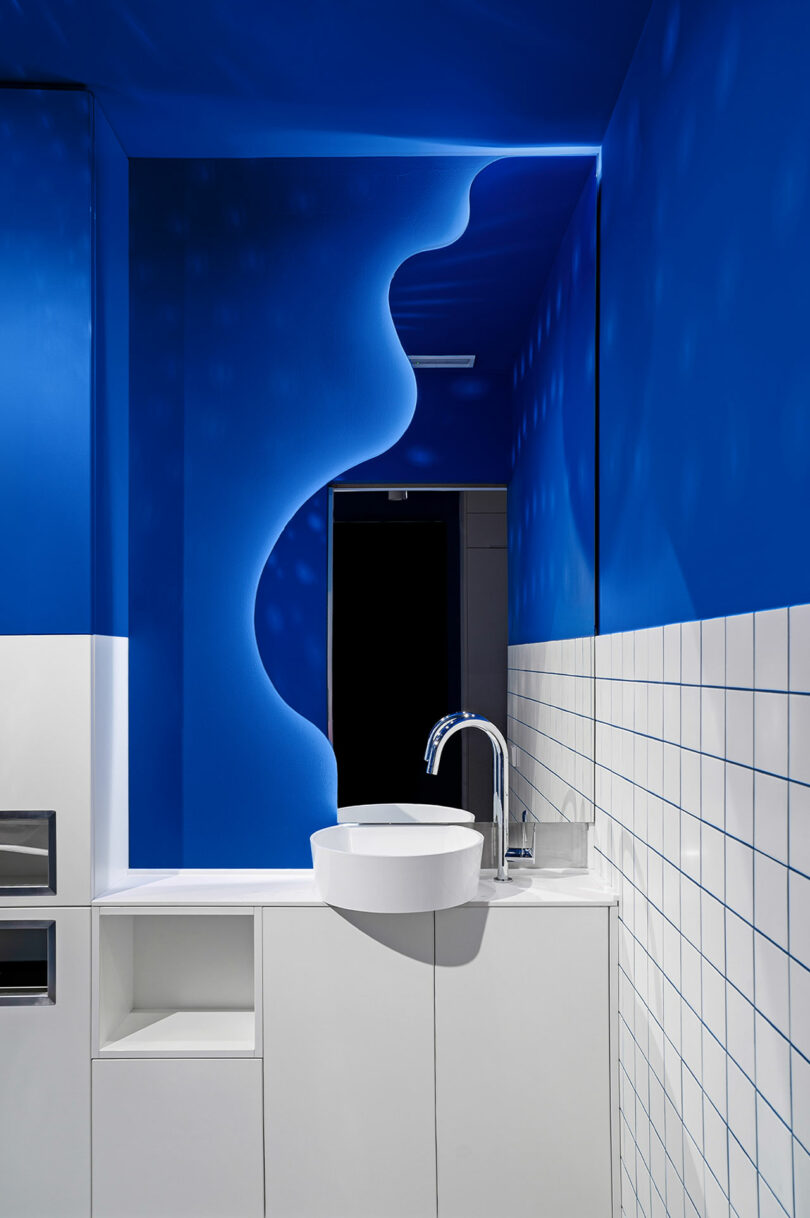 Modern bathroom with a unique blue wave-patterned wall, white sink, and tiled backsplash.