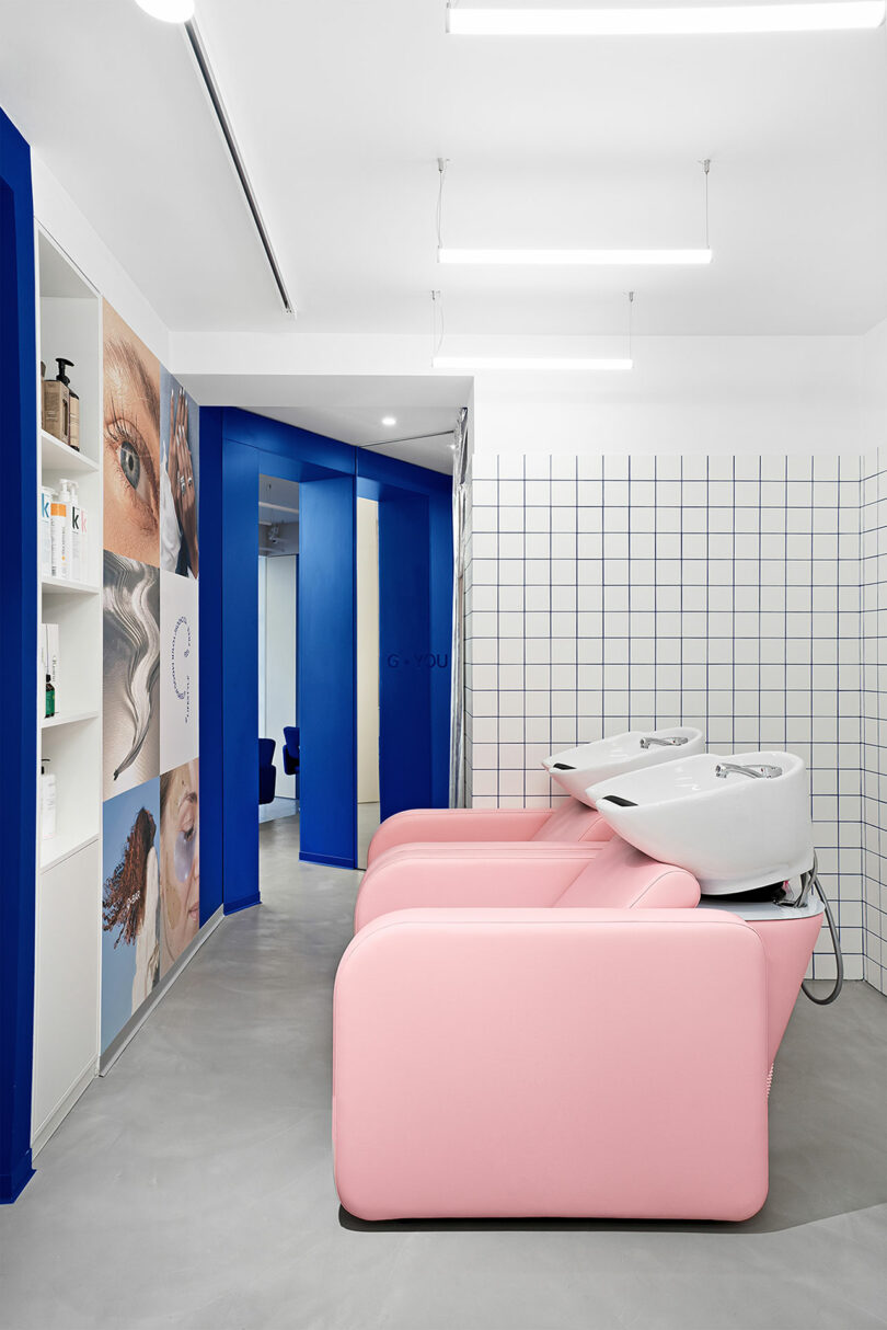 Salon interior with pink shampoo chairs, white washbasins, and a blue and white tiled wall. Display shelves hold hair products. Brightly lit with modern design elements.