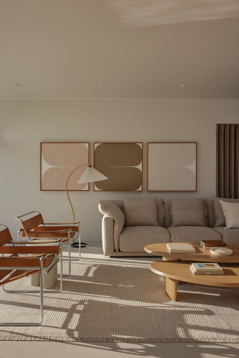 Cozy living room with a beige sofa, wooden coffee table, two leather chairs, and abstract art on the wall. Natural light fills the space.