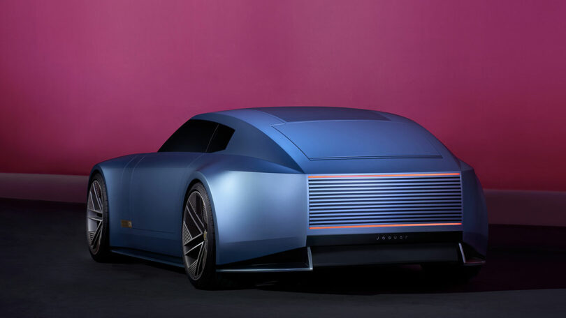 Futuristic blue concept car with sleek design and angular lines, displayed against a pink background.