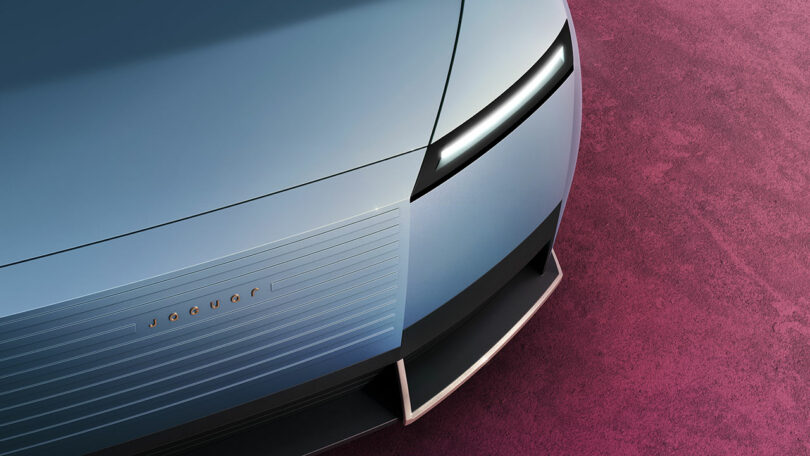 Close-up of a sleek, modern car's front with narrow headlights and a smooth grille, set against a textured pink background.