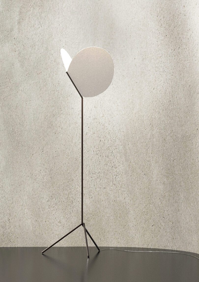 A minimalist floor lamp with a thin metal stand and a circular lampshade on a textured beige background