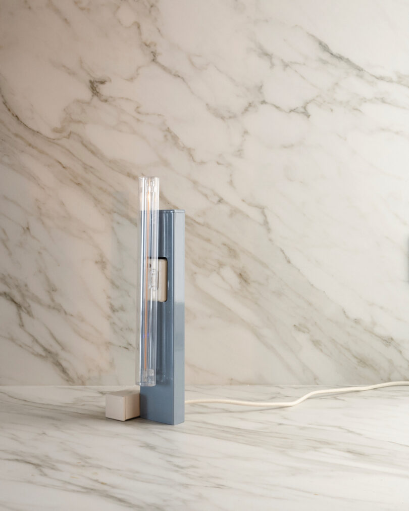 A sleek, modern blue and clear lamp sits on a marble surface with a marble background