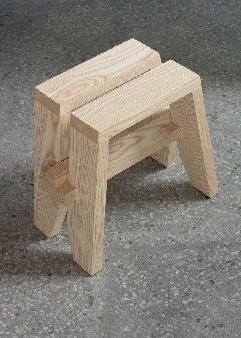 Two small wooden stools, each with simple, rectangular seats and four straight legs, are stacked on a terrazzo floor.