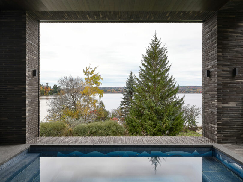 The view unfold from the covered patio—a shimmering pool bordered by brick walls, overlooking a placid lake and trees adorned in autumn's hues.