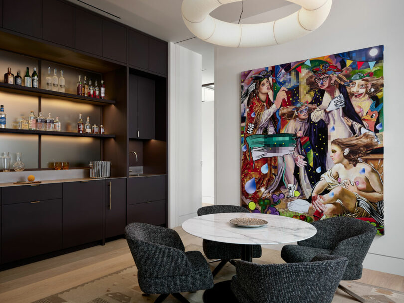 Contemporary dining area featuring a round marble table and four dark chairs complemented by a wall-mounted bar and a large colorful abstract painting on the wall.