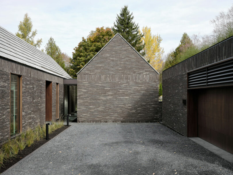 Modern home exterior featuring dark brick walls and a gravel courtyard, all embraced by the serenity of surrounding trees.