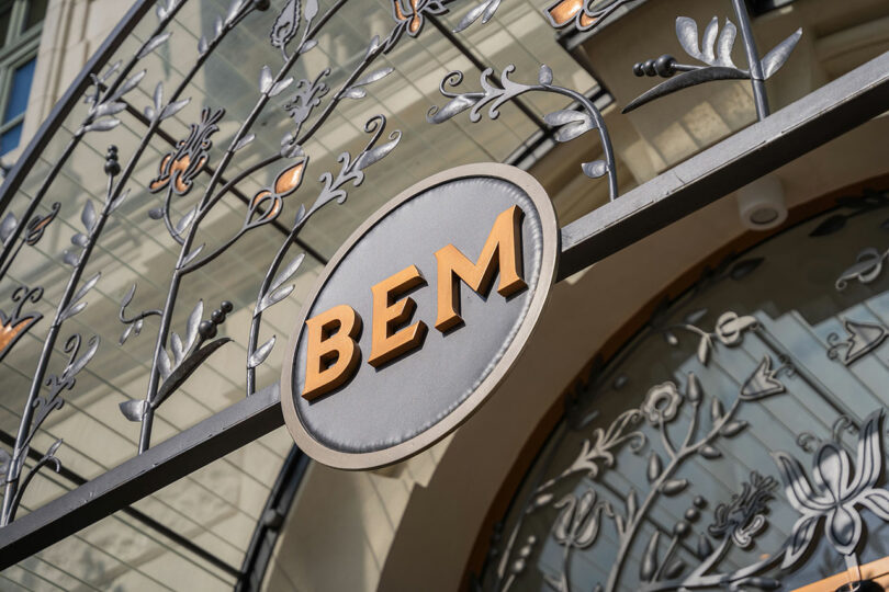 Outdoor metal sign with "BEM" in bold letters, surrounded by ornate floral designs.