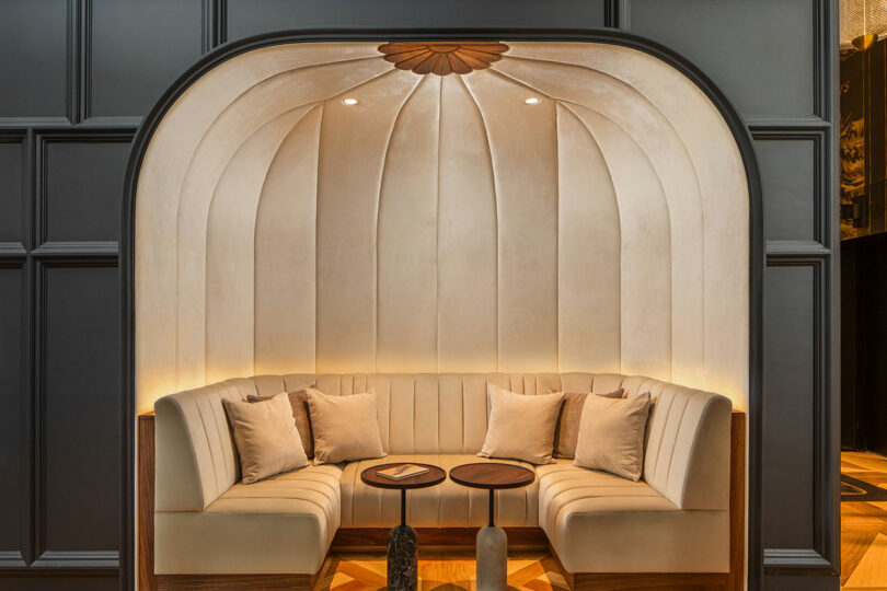 Cozy seating alcove with curved, upholstered walls, two small round tables, and accent pillows, lit gently from above.