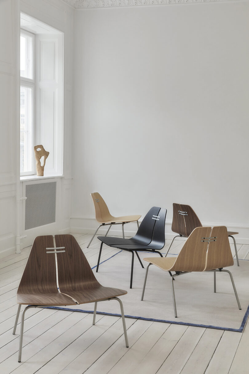 A group of modern chairs with sleek, minimalist designs arranged on a light wooden floor with a rug in a bright, white room. A sculpture stands on the window ledge.