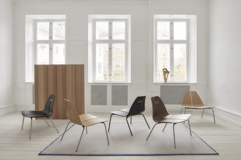 Minimalist room with six modern chairs, a light wood cabinet, large windows, and a sculpture on display.