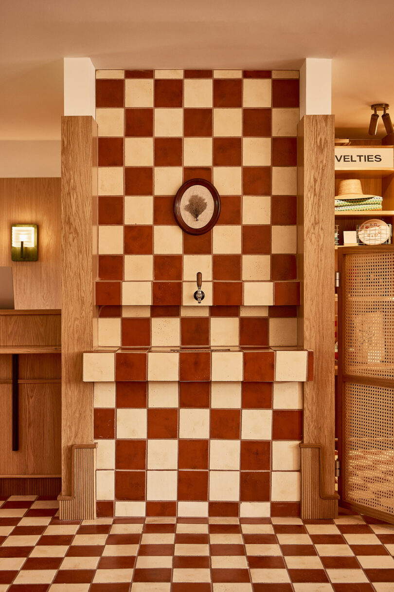 A checkerboard-patterned tiled wall, showcasing Parts and Labor Design's craftsmanship, features a small decorative faucet at its core. It's elegantly surrounded by wood paneling in a room bathed in warm lighting.