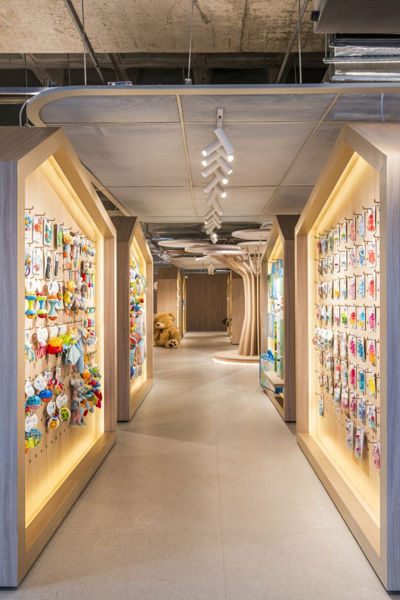 The brightly lit store aisle, featuring colorful children's toys on display shelves, reflects Moas Group's family of brands. The wooden floor and ceiling add a warm touch to the vibrant ambiance.