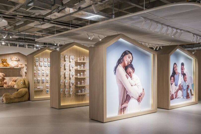 The Moas Group interior features product displays and large photos of families. Shelves are adorned with teddy bears and various packaged items, all under a ceiling of exposed ductwork and modern lighting.