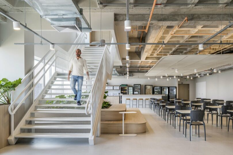 A man walks down a white staircase in the modern, open-plan Moas Group office, surrounded by sleek tables and chairs.