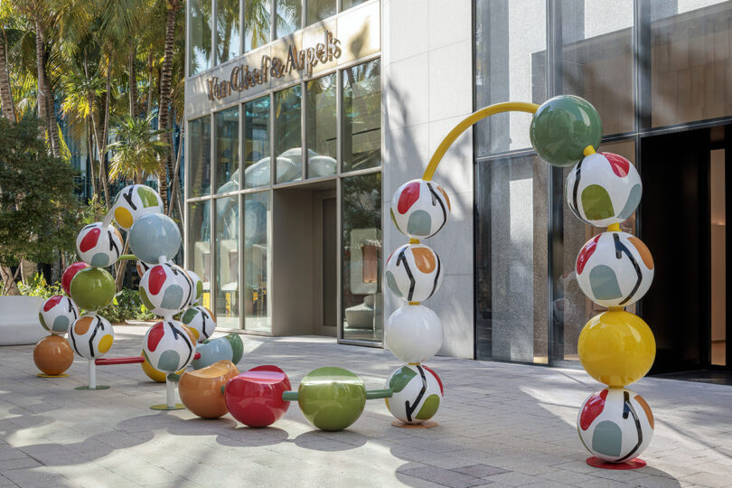 Colorful outdoor sculpture of interconnected large spheres stands in front of a building with a Van Cleef & Arpels sign.