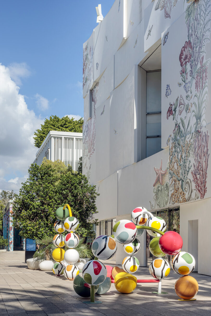 Modern building with artistic wall designs and colorful spherical sculptures outside on a sunny day.