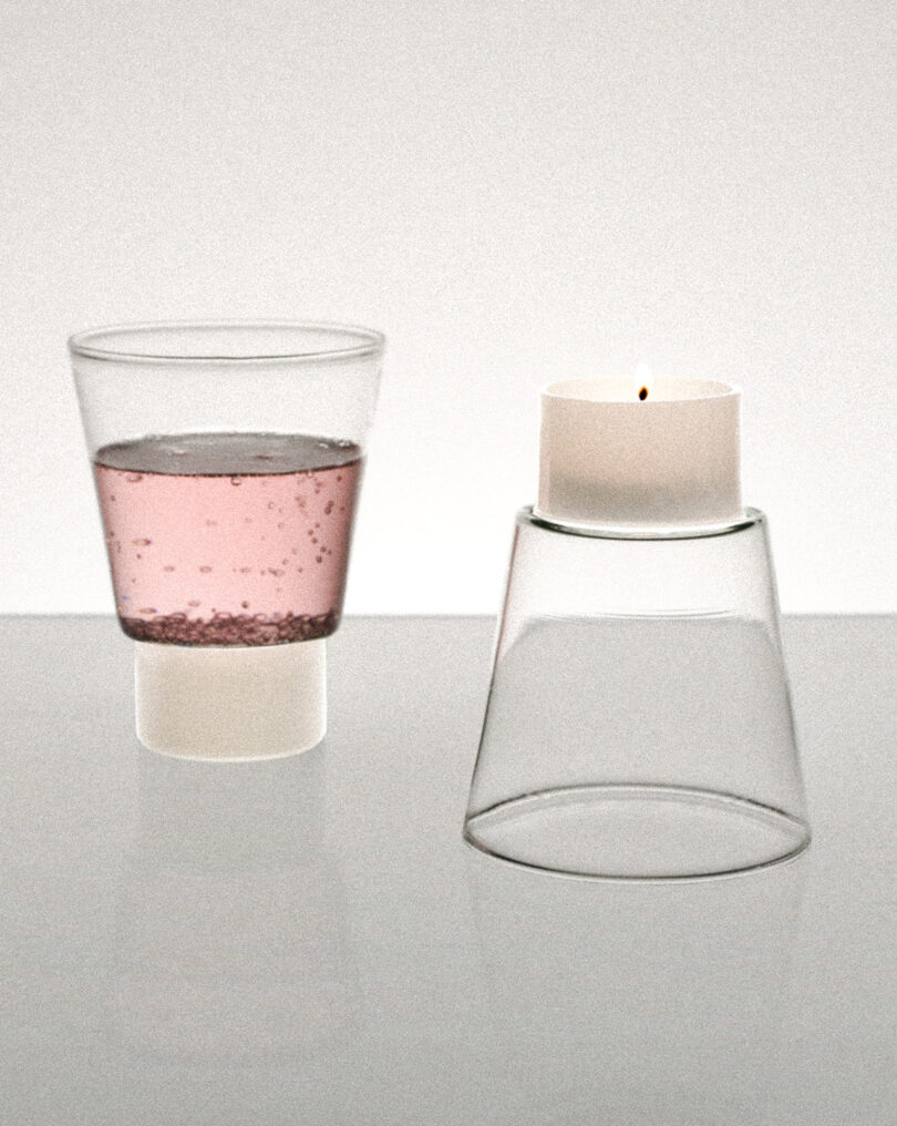 A glass with pink liquid on the left and an upside-down glass with a lit candle on top on the right, set against a plain background.