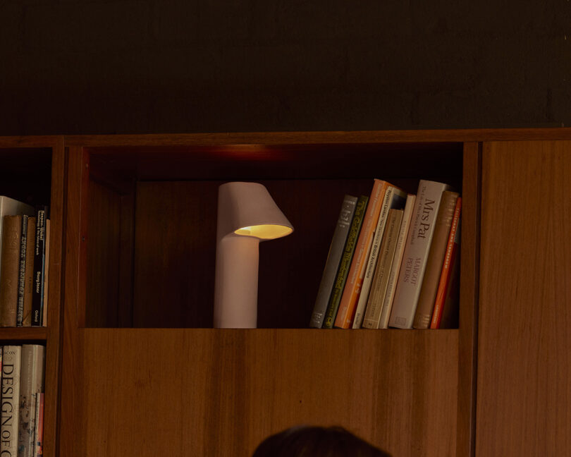 A wooden bookshelf with a small white lamp and several books in a cubby. The setting is dimly lit.